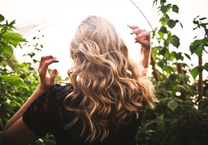 donna bionda con i capelli in piedi tra le piante verdi-1049687